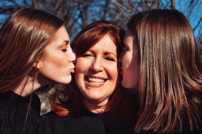 due ragazze baciano la mamma sulla guancia
